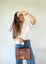 Cartera bandolera de cuero color marrón tostado, con doble asa corta y correa larga desmontable. Tiene un bolsillo frontal con cierre y un bolsillo interno.