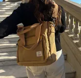 Bolso tipo tote de lona color beige con capacidad para notebook de 14 pulgadas. Posee cierre principal, bolsillo frontal con cierre y solapa, asas de mano y correa de hombro regulable y desmontable.