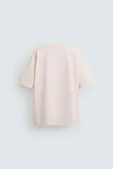 Camiseta color crema de corte holgado con cuello redondo y mangas cortas. Estampado frontal con la ilustración de un hombre sentado en un sillón.