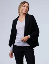 Cardigan negro de tejido suave, estilo poncho o capa, con cuello tipo chal y mangas amplias.