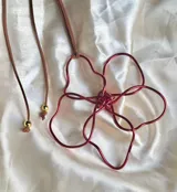 Collar con dije de flor de alambre rojo y cordón de gamuza marrón con detalles de cuentas doradas.