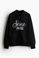 Campera negra con capucha y cierre frontal, con bolsillo tipo canguro y estampado blanco con la inscripción 'Seine Paris'.