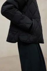 Campera acolchada de color verde militar con diseño de costuras en forma de diamante. Confeccionada en poliéster reciclado, presenta un cuello redondo, cierre frontal con botones a presión y mangas largas. Es una prenda repelente al agua de corte recto.