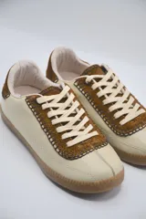 Zapatillas bajas color beige con detalles en marrón y cordones blancos.