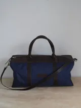 Bolso de lona color negro con detalles en cuero color tostado. Tiene doble asa de mano y correa de hombro ajustable y extraíble.