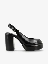 Zapato de tacón negro de charol, con punta redonda, plataforma delantera y correa con hebilla en el tobillo.