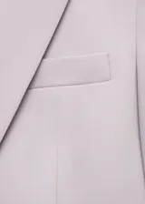 Blazer color beige con solapas de muesca, cierre frontal con un botón, hombros estructurados, corte entallado, forro interior y dos bolsillos de ribete en la parte delantera.