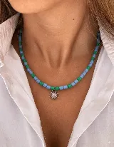 Collar corto con cuentas de cristal alternadas en color celeste y verde, con dije de sol plateado con incrustaciones de circonitas.