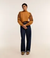 Sweater color ocre con cuello alto y mangas largas con sisas raglán. El sweater tiene bordados de flores en los laterales de las mangas.