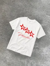 Remera blanca de algodón con cuello redondo y estampado frontal con tres estrellas rojas y la palabra "Plagstar" en cursiva.