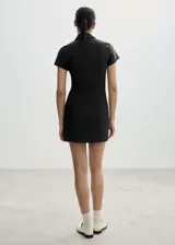 Minivestido negro de poliéster, viscosa y elastano, con cuello camisero, cierre frontal con cremallera, mangas cortas, corte entallado y costuras decorativas.