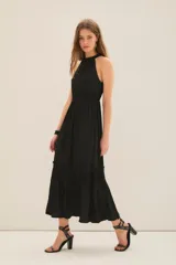 Vestido largo negro con escote halter con volados en cuello y fuelle con cinta interna para ajustar escote. Tiene volados y costuras elásticas en cintura y ruedo con volado.