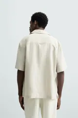 Camisa color marrón oscuro de corte relaxed fit, confeccionada en tejido de lino. Tiene cuello bowling, manga corta, bajo con aberturas laterales y cierre frontal de botonadura.