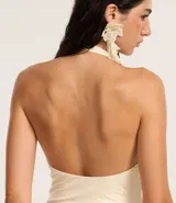 Vestido largo color crema, de tejido jersey, con escote halter y detalle de nudo/torcido en el busto que genera un recorte cutout central. El vestido es ajustado al cuerpo.