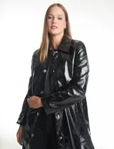 Chaqueta larga tipo trench de charol negro con acabado brillante e impermeable. Presenta cuello con solapa, cierre frontal con botones metálicos plateados y bolsillos laterales. Su diseño es de corte recto y estructura rígida.