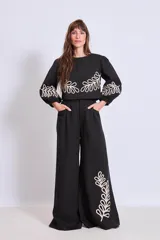 Blusa negra con cuello redondo y mangas largas abullonadas, con apliques bordados de hojas en color crudo en el frente y en las mangas.