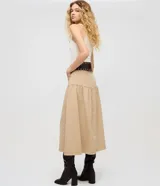 Pollera midi color beige confeccionada en sarga de algodón certificado BCI, con cintura alta y pasadores, bolsillos frontales, recorte en la cadera con frunces y cierre de botón y cremallera.