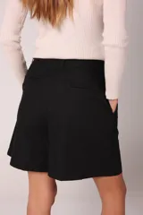 Bermuda color crema de lino con tiro alto, elástico en la parte trasera de la cintura, bolsillos delanteros y cierre frontal con cremallera y botón.