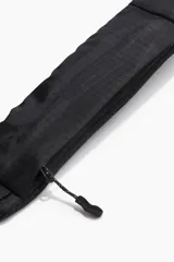 Bolso cruzado de deporte negro en tejido grueso. Tiene un compartimento grande con cierre y cordón elástico entrelazado adelante con tope de plástico. La correa es ajustable y levemente acolchada, con un compartimento de cierre atrás, argolla en D adelante y hebilla de plástico.