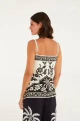Top sin mangas color blanco con estampado de flores y hojas en negro. Tiene tirantes finos ajustables y lazo en la parte delantera.