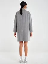 Tapado de largo medio, color gris, con aplicaciones de strass distribuidas por toda la prenda. Presenta cuello solapa, cierre frontal con broches ocultos y bolsillos integrados.