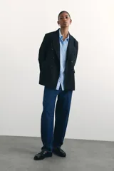 Camisa celeste de algodón suave, de corte holgado, con cuello clásico, botones frontales, canesú en la espalda, hombros caídos, bolsillo de parche en el pecho, mangas largas con puños abotonados y bajo redondeado.