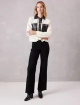 Chaqueta de corte boxy en color crema, confeccionada en tejido de punto suave con detalles en cuero sintético negro en cuello, solapas, cartera frontal y bolsillos. Presenta cierre frontal con botones metálicos plateados, hombros caídos y costuras decorativas horizontales.