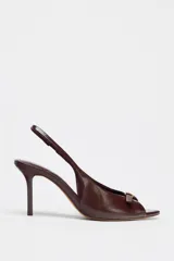 Zapato tipo sandalia destalonada color marrón chocolate, con tacón fino, tira delantera con detalle de hebilla metálica dorada y tira trasera elástica.