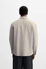 Camisa color crema de corte relaxed fit, confeccionada en tejido de mezcla de algodón suave al tacto. Tiene cuello solapa, manga larga con puños abotonados, un bolsillo de parche en el pecho y cierre frontal con botones.