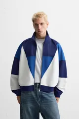 Chaqueta deportiva azul marino, azul y blanca con cierre frontal, cuello alto y bolsillos laterales.