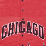 Camiseta deportiva roja de básquet, con cuello y mangas con ribete blanco y negro. Estampado frontal con el nombre "Chicago" en letras negras con borde blanco y el logo del equipo Chicago Bulls. Cierre frontal con botones a presión.