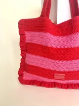 Bolso tipo tote tejido a crochet, con hilo 100% algodón, a rayas horizontales color crema y lila, con volados en los bordes y manijas reforzadas.