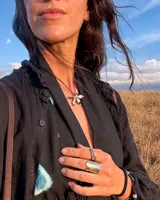 Collar artesanal con dije de flor plateada, realizado con hilo de seda natural teñido a mano.