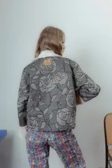 Chaqueta corta gris con estampado de rosas negras, cuello y puños de piel sintética blanca, cierre frontal con cremallera y bolsillos delanteros con solapa.