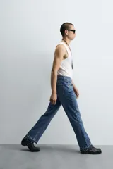 Pantalón de jean celeste de corte flare, con tiro medio, cinco bolsillos, cierre frontal con cremallera y botón, y bajo con acabado irregular.