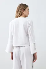 Blusa blanca de lino con escote en V y cierre frontal con lazos. Mangas largas acampanadas.