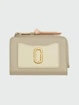 Billetera Marc Jacobs modelo The Utility Snapshot Slim Bifold, de cuero color beige con aplique frontal en cuero color crema y logo dorado. Tiene cierre perimetral con tirador de cuero rosa.