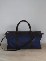 Bolso de lona azul con detalles en cuero marrón, doble asa de mano y correa bandolera ajustable. Incluye un neceser haciendo juego con cierre y logo de caballo bordado.