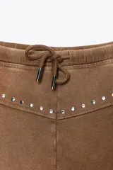 Shorts color marrón de algodón con efecto lavado, tiro medio, cintura elástica ajustable con cordones y detalle de tachas plateadas.