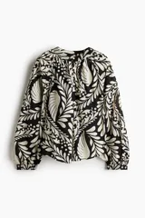 Blusa oversized de algodón y viscosa con estampado de hojas y lunares en blanco y negro. Tiene cuello mao, abertura frontal con botones forrados, mangas globo largas con puños abotonados y bajo redondeado.