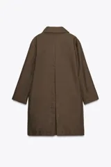 Trench color marrón con cuello solapa y manga tres cuartos. Tiene bolsillos delanteros y cierre frontal con cremallera y botones ocultos por solapa.