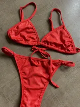 Conjunto de bikini rojo con textura acanalada, compuesto por corpiño triangular con tirantes finos regulables y bombacha tipo colaless con tiras laterales ajustables.