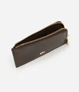 Billetera pequeña de material sintético color marrón oscuro, con cierre de cremallera metálica dorada en el borde superior y logo grabado en dorado "STN" en la parte frontal.