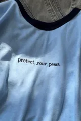 Remera blanca de algodón con ribete amarillo en cuello y mangas, y frase bordada en color naranja.