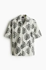 Camisa de manga corta con estampado de hojas en tonos grises sobre fondo blanco. Tiene cuello resort, tapeta lisa y corte regular.