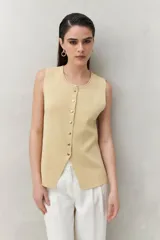 Chaleco tejido color crema con botones al frente y abertura inferior.