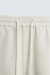 Pantalón color arena de corte recto, confeccionado en tejido de algodón y lino. Cuenta con cintura elástica ajustable con cordón, bolsillos delanteros y traseros de parche.