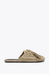 Zapato plano destalonado tipo mule, color beige, confeccionado en serraje. Presenta antifaz y lazo con borlas en la parte delantera.