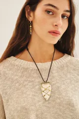 Collar con dije en forma de escudo de hueso con detalles dorados, colgando de un cordón negro ajustable.