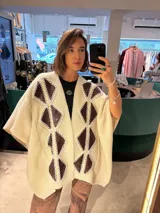 Ruana color crema tejida en punto grueso con apliques de cuero marrón en forma de rombos.